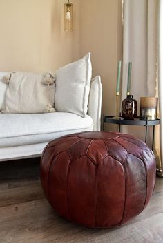 a living room with a white couch and brown ottoman on the floor in front of a window