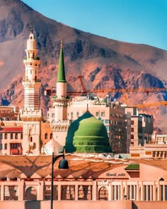 a large green dome on top of a building next to tall buildings with mountains in the background