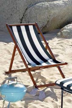 an empty beach chair sitting on the sand next to a blue and white lawn chair