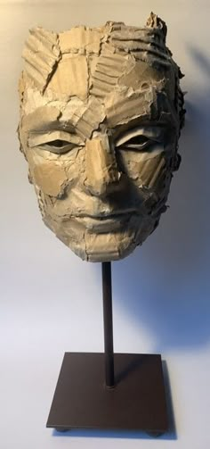 a clay head on a stand in front of a white wall