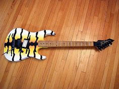 an electric guitar painted with black and yellow stripes on a wood flooring surface,