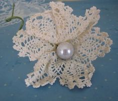 a white lace flower with a pearl on the center sits on a blue tablecloth