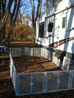 an rv parked in the woods next to a white fence