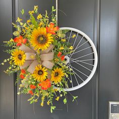 a wreath with sunflowers and other flowers hanging from the front door on a bicycle wheel