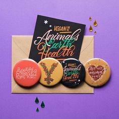 four buttons with the words vegan and animals for health written on them are in an envelope