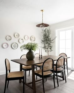 a dining room table with chairs and plates on the wall behind it, along with a vase filled with flowers