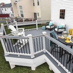 an outdoor deck with chairs and table on the grass next to a white house in the background