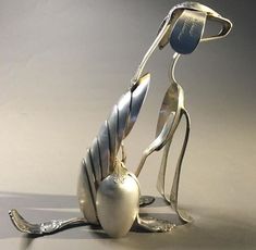 a silver sculpture sitting on the ground with its legs spread out and hands extended to it's sides