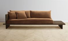 a brown couch sitting on top of a wooden floor next to a white wall in an empty room