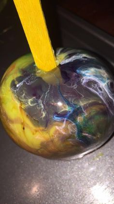 a yellow toothbrush sticking out of a marbled apple with black and blue swirls