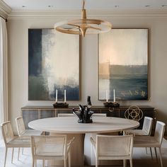 a dining room table and chairs with artwork on the wall behind it in front of two large paintings