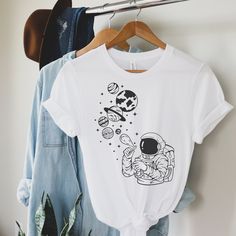 a white t - shirt with an astronaut on it hanging from a clothes hanger