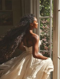 a woman in a white dress looking out the window with long, flowing hair on her head