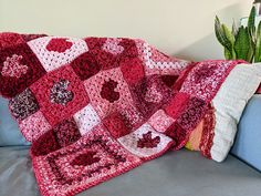 a crocheted blanket sitting on top of a couch next to a potted plant