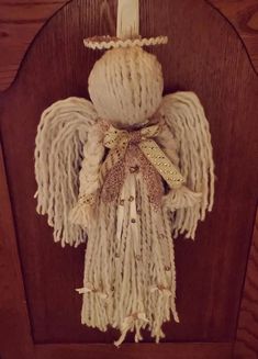 an angel made out of yarn hanging on a wooden frame with ribbon around it's neck