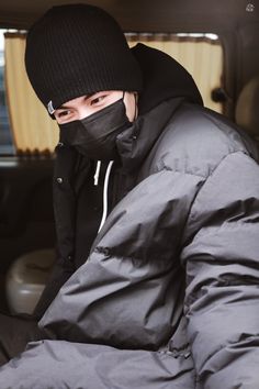 a man sitting in the back of a car wearing a black face mask and jacket