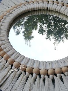 a circular mirror with tassels hanging from it's sides and a tree in the background