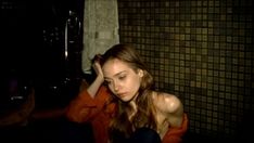 a young woman sitting in front of a sink with her hand on her head and looking at the camera