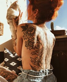 a woman with tattoos on her back holding a cat and looking out the window at the sky