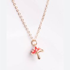 a gold necklace with a red mushroom charm hanging from it's center, on a white background