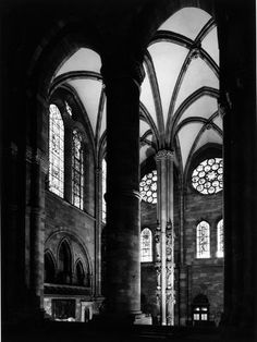 black and white photograph of the inside of a church with high vaulted ceilings, stained glass windows, and stone pillars