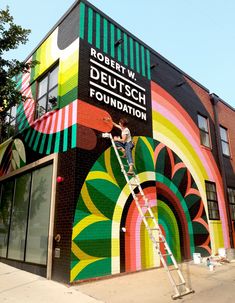 a man is painting the side of a building with bright colors and he is on a ladder