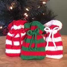 three knitted christmas bags sitting on top of a table next to a christmas tree