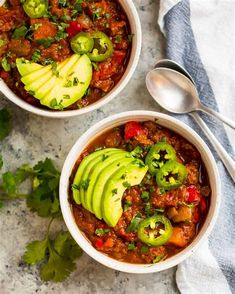 two white bowls filled with chili and avocado