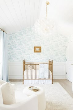 a baby's room with blue and white wallpaper, a gold crib and chandelier