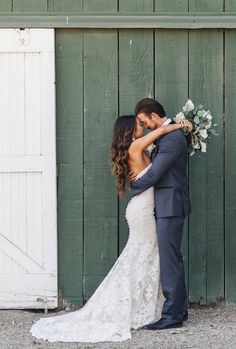 a bride and groom standing in front of a green barn door with their arms around each other