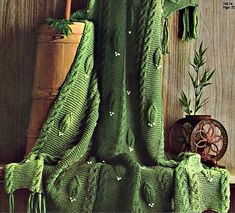 a green knitted blanket sitting on top of a wooden table next to a potted plant