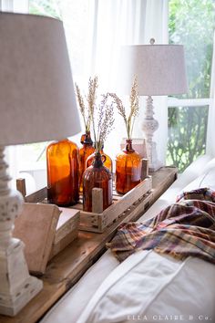 three orange glass bottles sitting on top of a wooden tray next to a lamp and window