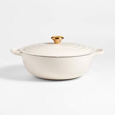 a white casserole dish with a gold handle on the top and an open lid