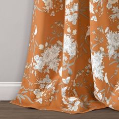 an orange and white flowered curtain hanging on a wall next to a wooden floor