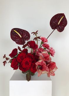 a vase filled with red and pink flowers on top of a white table next to a wall