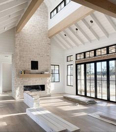 an empty living room with wood flooring and white brick fireplace in the center, surrounded by large windows