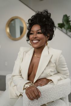 a woman sitting on top of a white chair in front of a mirror and smiling