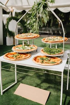 several pizzas sitting on top of a white table under a tent with greenery