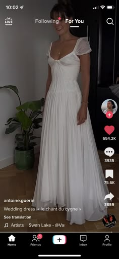 a woman in a white dress standing next to a plant