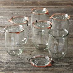 six clear glass jars with copper lids on a wooden table, one is empty and the other has no lid