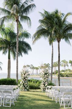 an outdoor ceremony with white chairs and palm trees