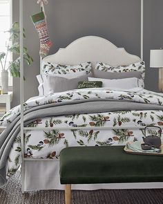 a bed with white sheets and pine cones on it, next to a green foot stool