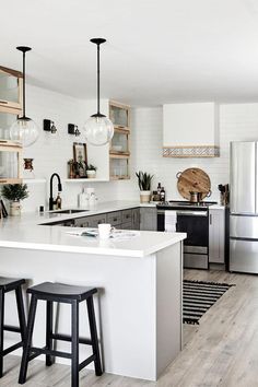 a white kitchen with two stools next to an island in front of the sink