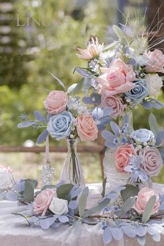 flowers in vases sitting on a table with greenery and candlesticks next to them