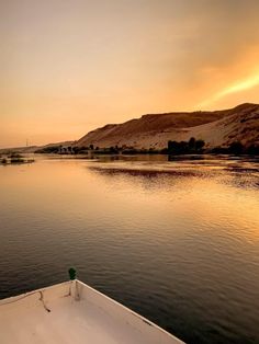 the sun is setting over a body of water with hills in the distance and trees on either side