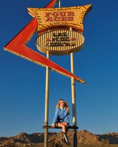 a woman sitting on top of a wooden sign in front of a desert area with mountains