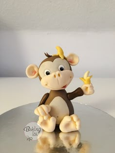 a monkey figurine holding a banana on top of a silver table with white walls