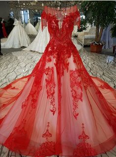 a red wedding dress on display at a bridal event in an indoor area with people walking around