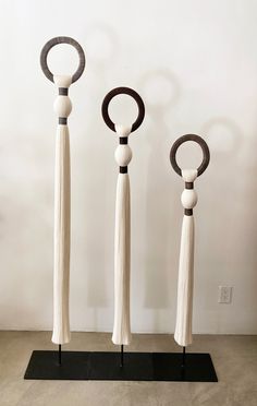 three wooden sculptures with tassels and rings on top of each other in front of a white wall