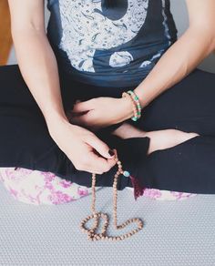 a woman sitting in a lotus position with her hands on the ground, wearing bracelets